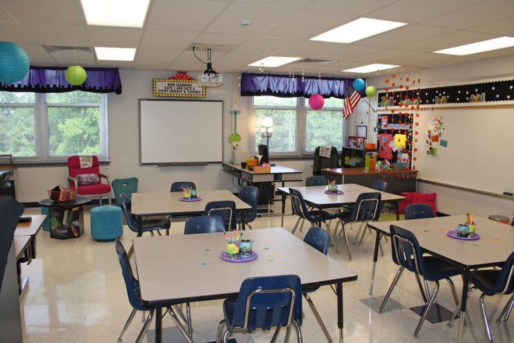 An empty primary school classroom with a number of square tables and four plastic chairs around each one.