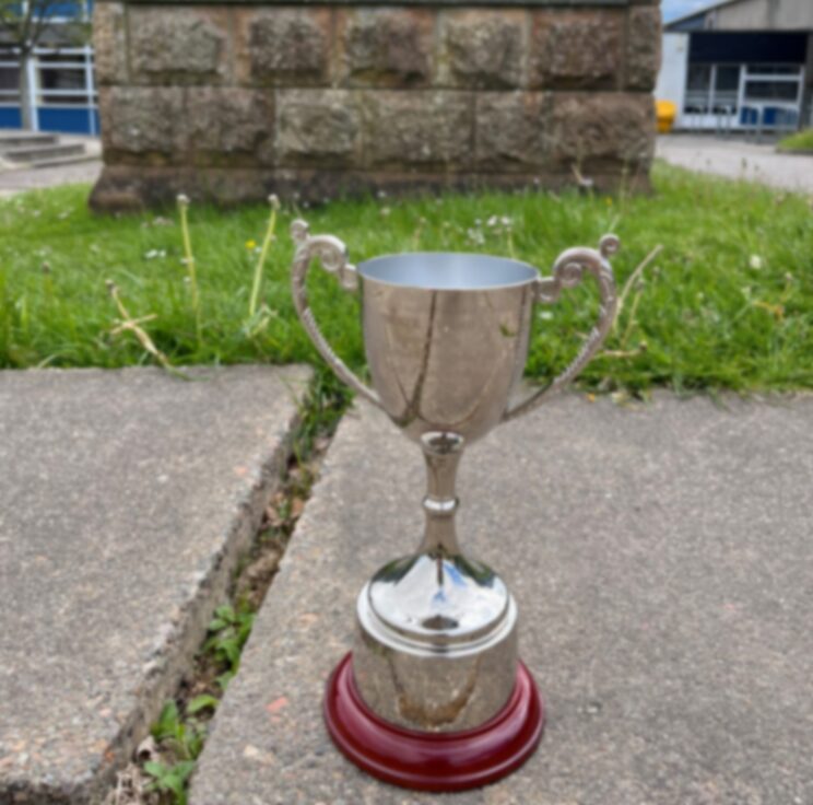 A metal trophy sitting on a pavement within a school setting.